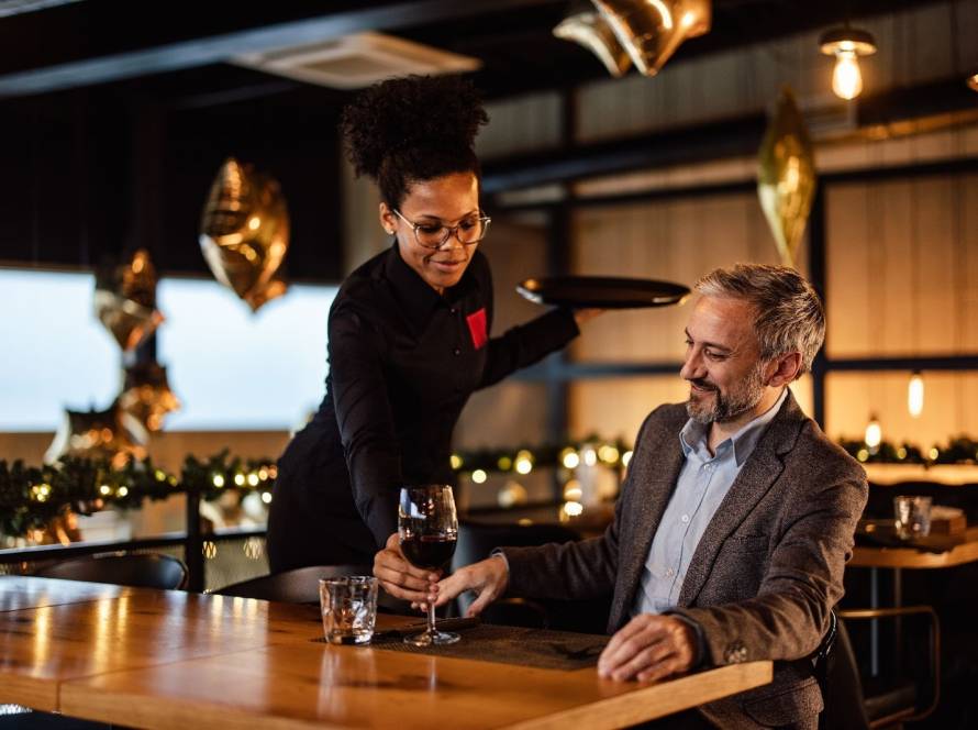 Waitress serving wine to a happy gentleman in an elegant bar and restaurant
