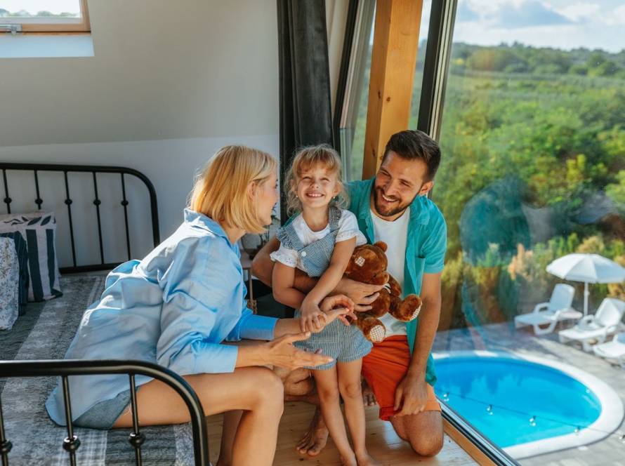 A family of three enjoying quality time inside a vacation rental that overlooks a sparkling outdoor pool.