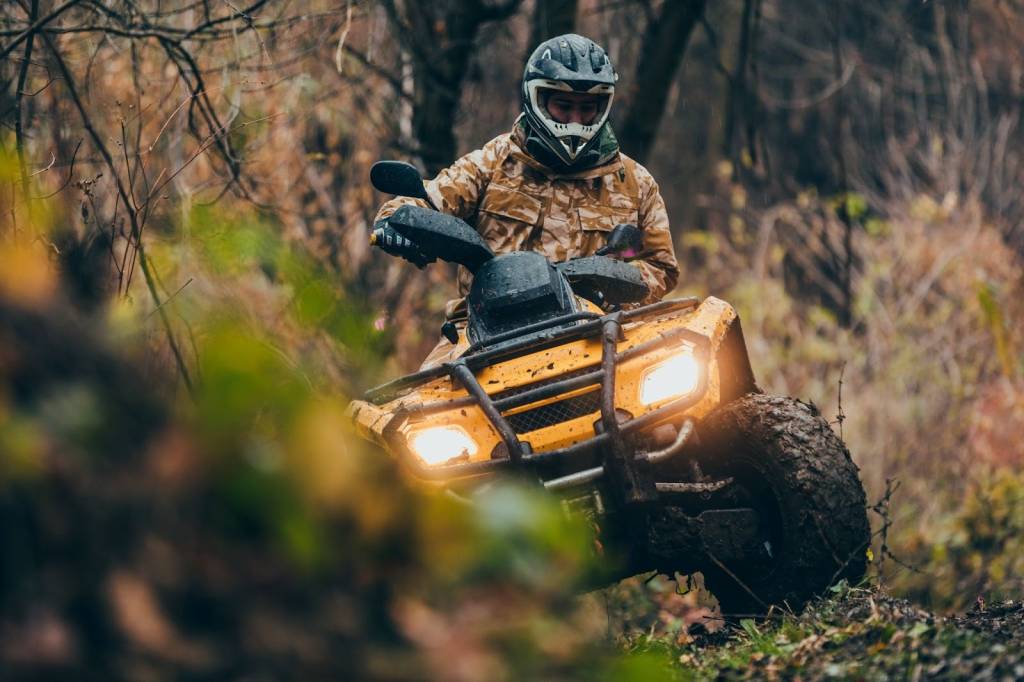Rider wearing full safety gear driving an ATV four-wheeler on a dirt path