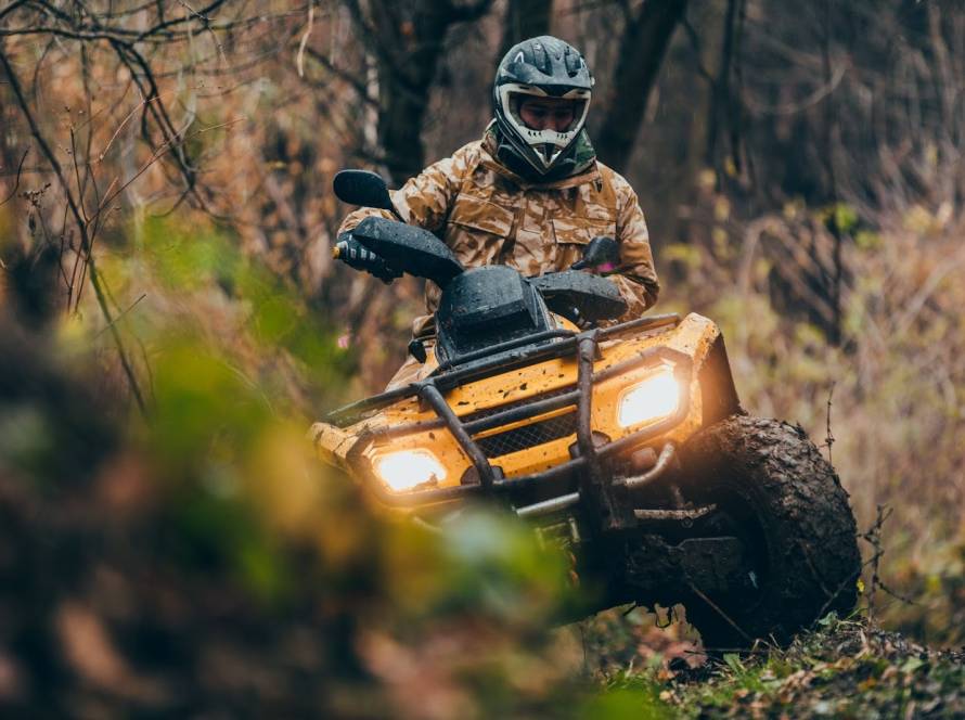 Rider wearing full safety gear driving an ATV four-wheeler on a dirt path