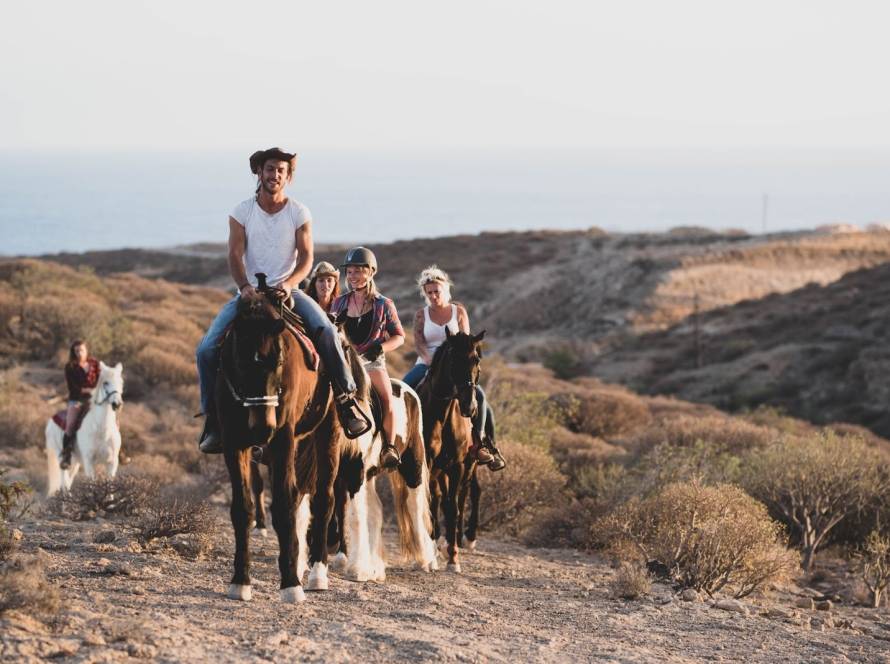 Tourists enjoying a guided horseback riding tour along a countryside path