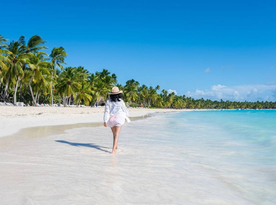 Woman walking along a sandy beach in the Dominican Republic with turquoise water and palm trees