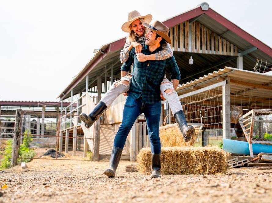 Playful engagement photo idea of a woman riding piggyback on her partner outdoors on a ranch
