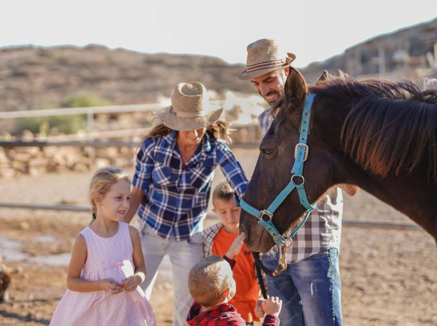 Couple with their little kids enjoying their time petting a horse during their vacation at a ranch resort